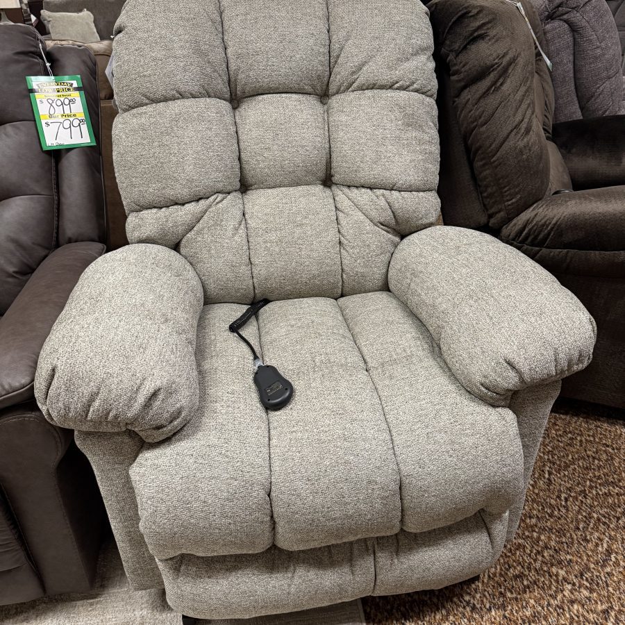 Gray textured recliner in a furniture store, tufted cushions, with a power cord on the seat and a price tag hanging from the arm.