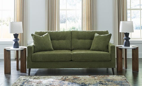 Green sofa with three matching cushions centered in a bright living room, flanked by wooden side tables and matching lamps on each side.