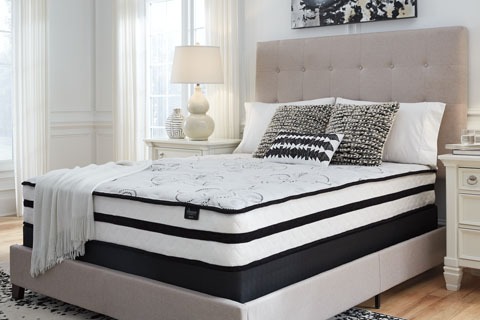 Queen bed with a light gray upholstered, tufted headboard, white bedding, and decorative pillows in a bright bedroom.
